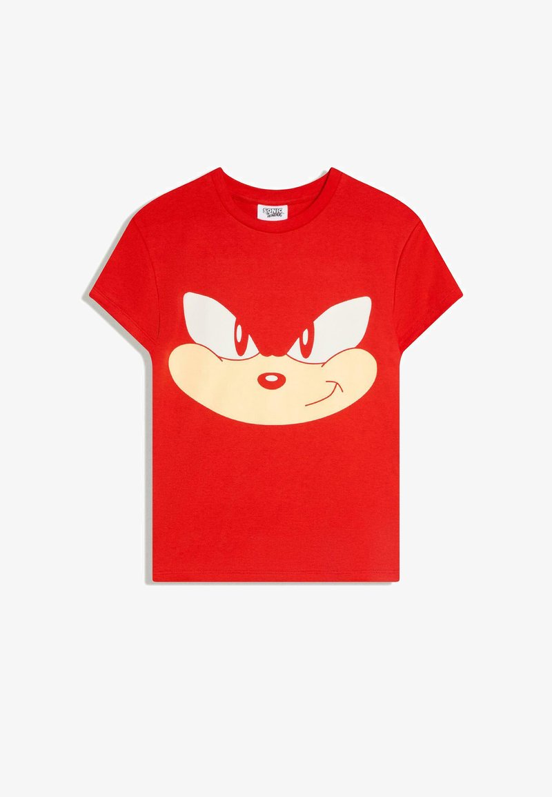 T-shirt rouge à manches courtes arborant un grand visage stylisé de Sonic le Hérisson avec des yeux déterminés et une bouche souriante sur le devant.