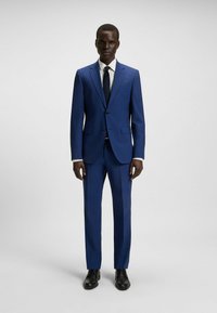 Blauw pak met een gesneden pasvorm, enkel-breasted jasje, wit overhemd met stippen, marineblauwe stropdas en zwarte nette schoenen.