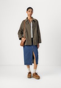 Olivově zelená bunda s límcem, bílý pletený top, modrá džínsová sukně s předním rozparkem, béžové boty se šněrováním a hn ědá crossbody taška.