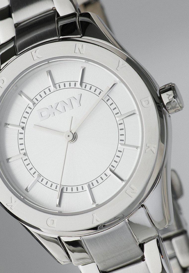 DKNY-Uhr mit einem silberfarbenen Metallarmband, rundem weißen Zifferblatt, minimalistischen Stundenmarkierungen und dem Markenlogo in der Mitte.
