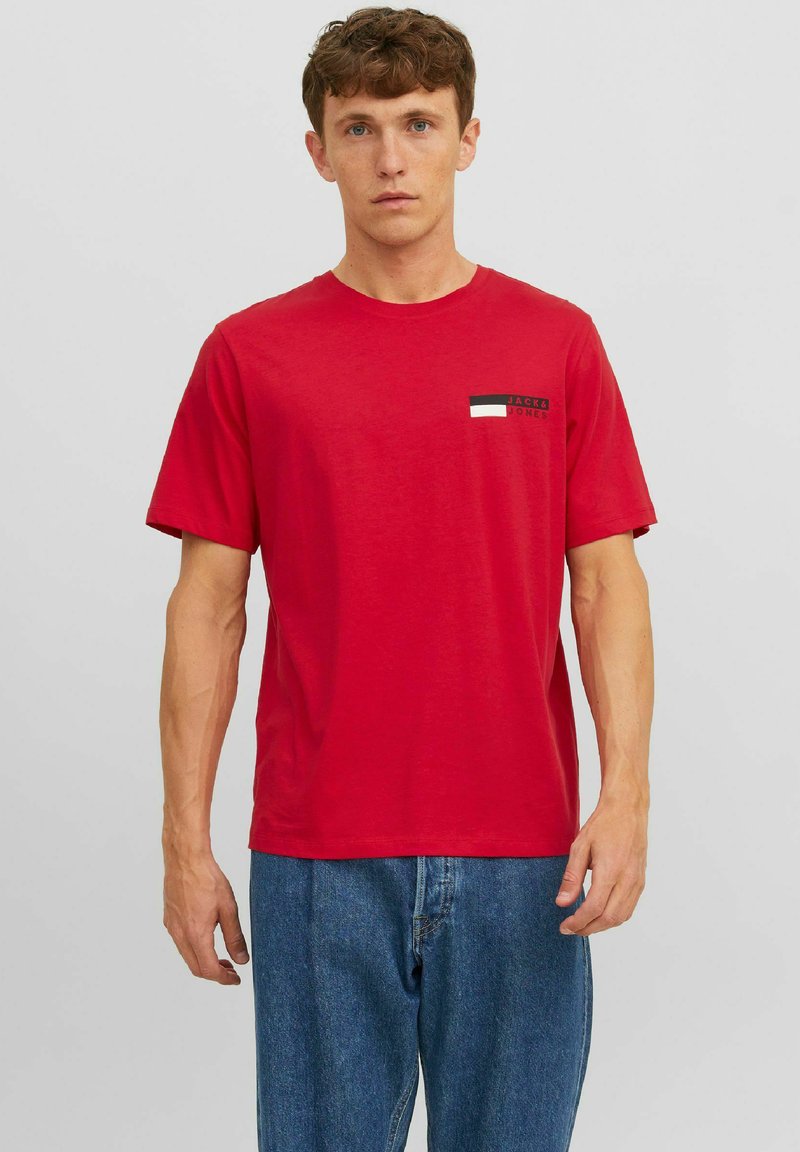 Rode katoenen t-shirt met korte mouwen en ronde hals. Heeft een klein rechthoekig grafisch detail in zwart, wit en groen op de borst.