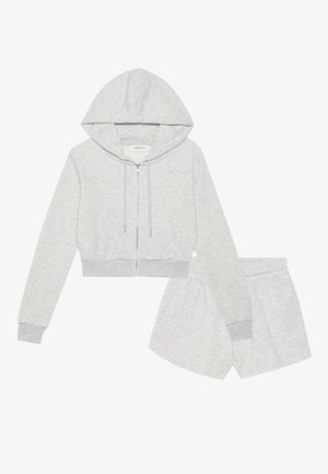 Svijetlosiva skraćena hoodie s kapuljačom, vezicom i prednjim džepovima, u kombinaciji s odgovarajućim šortsevima s elastičnom gumicom i glatkom teksturom.