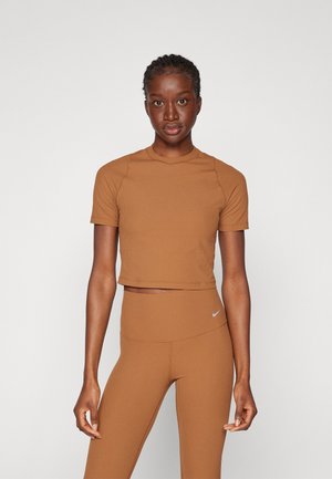 Brun ribbet crop-top med korte ermer, sammen med høyt liv matchende tights med en liten Nike-logo. Glatt tekstur.