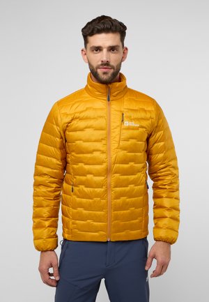 Geel pufferjack met een quiltpatroon, hoge kraag en rits aan de voorkant. Heeft een logo op de borst en is gecombineerd met donkere broeken.