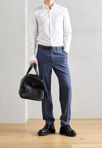 Witte blouse met knopen, blauwe broek, zwarte leren schoenen en een zwarte tas met een cirkelvormig handvat. Glad materiaal, nauwsluitende pasvorm, gestructureerd ontwerp.