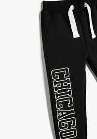 Pantalones deportivos negros con cordón blanco, que cuentan con bolsillos laterales y un gran gráfico "CHICAGO" en blanco en la pierna izquierda. Material suave de mezcla de algodón.