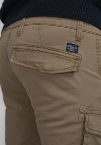Beige cargobroek van een zachte, gestructureerde stof. Voorzien van een achterzak met een label, dubbelgestikte naden en een losse pasvorm.