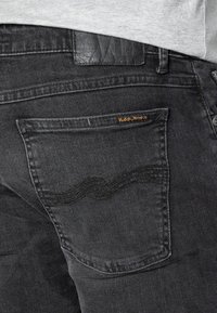 Svarta denimjeans med en strukturerad yta. Funktioner en bakficka med böljande sömmar och en logolapp. Diskret kontrastsöm.