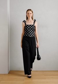 Black polka dot tank top with knotted straps paired with loose black trousers; model carries a small black handbag and wears black heels.
