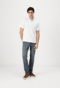 Hvid kortærmet polo shirt med krave og tre sorte knapper, kombineret med lyseblå jeans og brune sneakers. Glat stof, afslappet pasform.