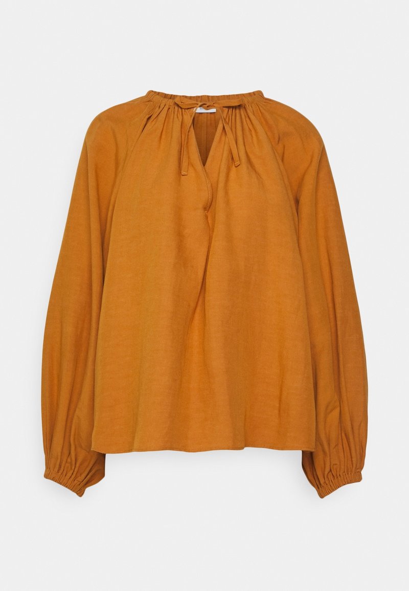 Blouse à manches longues couleur moutarde-orange avec un col froncé et fermeture à nouer, poignets élastiques et tissu léger et fluide.