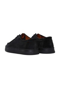 Zapatillas de ante negras con suela de goma texturizada negra, punta redondeada y diseño minimalista. El interior cuenta con un forro de cuero marrón.