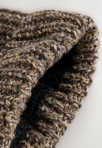 Căciulă tricotată din fir gros, de culoare maro, cu fire multicolore. Are o margine ribbată și o căptușeală interioară moale, de culoare neagră. Suprafață texturată.