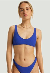 Blauwe geribbelde bikinitop met brede bandjes en een ronde halslijn, gepaard met bijpassende low-rise bikinitaille. Textuurstofdetail.