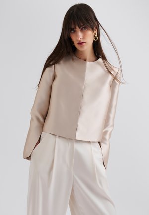 Lyse beige cropped jakke laget av satin, med rund hals og lange ermer, kombinert med kremfargede plissert bukser.