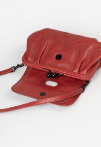 Red leather crossbody bag with a pleated design, flap closure, and black hardware. Features a thin strap and a smooth texture.