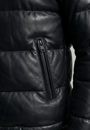 Sektion af sort polstret læderjakke, der viser lodret lynlås-lomme og en del af ærmet.