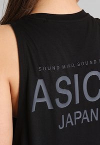 Černé bezrukávové tričko z měkké tkaniny, na kterém je velký potisk s textem "ASICS JAPAN" a "SOUND MIND, SOUND BODY" v šedé barvě.