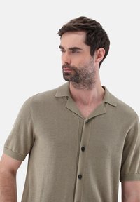 Maglietta a maniche corte di colore verde oliva in maglia, con colletto a camicia, bottoni neri e finitura testurizzata. Design pulito e casual.