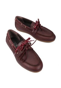 Brązowe skórzane buty żeglarskie z okrągłym noskiem, kontrastującymi bordowymi sznurówkami, złotymi oczkami i gumową podeszwą z dokładnym przeszyciem.