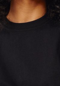 Camiseta de algodón negra con cuello redondo y mangas cortas. La tela es suave y tiene una fina textura acanalada.