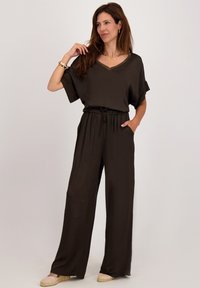 Donkerbruine jumpsuit van soepel stof, met een V-hals, korte mouwen, een elastische tailleband en zijzakken.