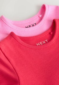 Dva majice u ružičastoj i crvenoj boji, s rebrastom teksturom i okruglim izrezima. Logotipi prikazani na unutarnjoj ovratniku svake majice.