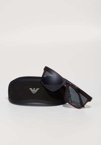 Ochelari de soare din scoică cu lentile întunecate, formă rectangulară înclinată, cu un strat anti-reflexie, păstrați într-un toc moale negru cu logo.