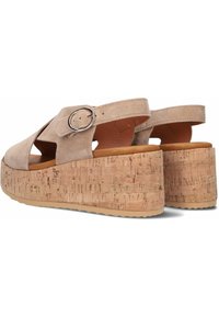 Bottes compensées en suede beige avec plateforme en liège, bride de cheville réglable et détail en boucle argentée, caractérisées par une surface texturée et une base solide.