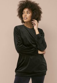 Top de terciopelo negro de manga larga con cuello redondo, ajuste relajado y superficie texturizada. Presenta mangas con volantes y un acabado suave.