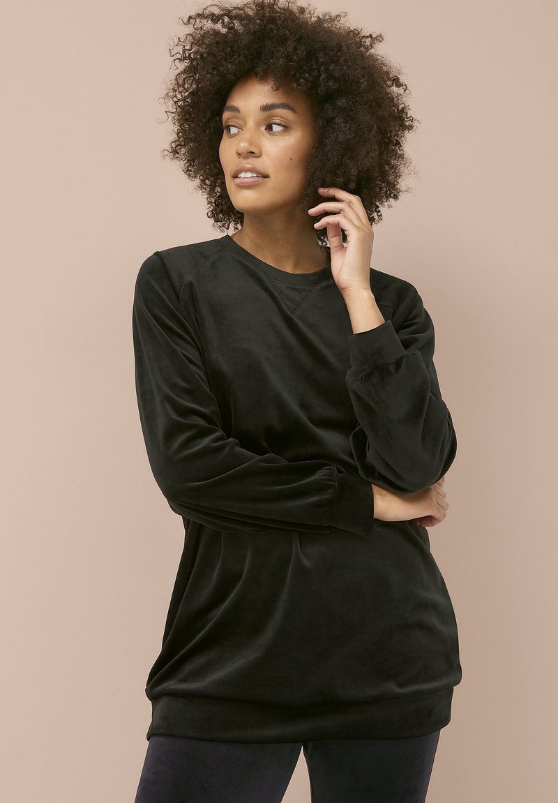 Top de terciopelo negro de manga larga con cuello redondo, ajuste relajado y superficie texturizada. Presenta mangas con volantes y un acabado suave.