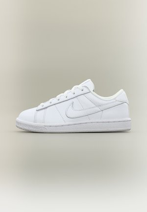Biele nízke tenisky Nike so šnúrkami, vyšitým logom na boku a textúrovanou podrážkou na neutrálnom pozadí.