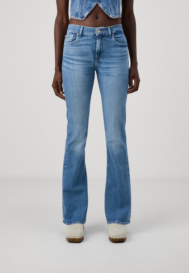 Lichtblauwe flared jeans met een medium hoge taille, denim textuur, subtiele vervaging en gestikte accenten bij de zakken en de zoom. Gecombineerd met klompen.