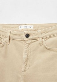 Ceinture de pantalon beige avec fermeture par bouton, passants pour ceinture, poches avant et étiquette de vêtement avec information sur la taille.