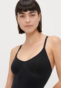 Μαύρο αόρατο σουτιέν με λεπτές ρυθμιζόμενες τιράντες, ελαφριά επένδυση και λεία υφή, που διαθέτει μια διακριτική σχεδίαση. Κοντινή λήψη.