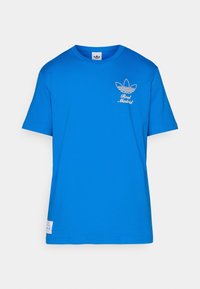 Blue short-sleeve cotton t-shirt featuring a white graphic of the Adidas logo and "Real Madrid" text on the left chest area.