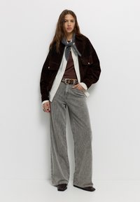 Bruine suède jas, witte blouse, bruine top, grijze corduroy wijde broek, grijze sjaal, zilveren riemgesp, zwarte enkellaarsjes.