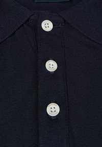Marineblauwe polo met een textuurgebreide stof, voorzien van een kraag en drie witte knopen met zwarte gaten en een reliëf merknaamdetail.
