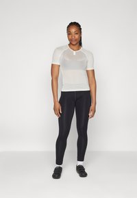 Weißes Mesh-T-Shirt mit kurzen Ärmeln und einem Schlüsselloch-Ausschnitt, kombiniert mit schwarzen, figurbetonten Leggings. Das Outfit ist für sportliche Aktivitäten konzipiert.