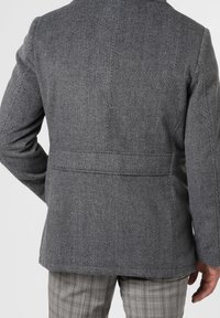 Blazer in lana grigia a spina di pesce con una vestibilità strutturata, apertura centrale e dettagli di cucitura minimalisti, abbinato a pantaloni a quadri.
