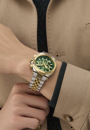 Reloj de acero inoxidable dorado y plateado con un dial verde, características de cronógrafo, marcadores de hora audaces y bisel texturizado, llevado en una muñeca.