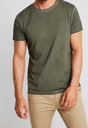 Olivengrøn kortærmet t-shirt lavet af blødt, glat materiale med rund halsudskæring og tætsiddende pasform, kombineret med lysebeige bukser.