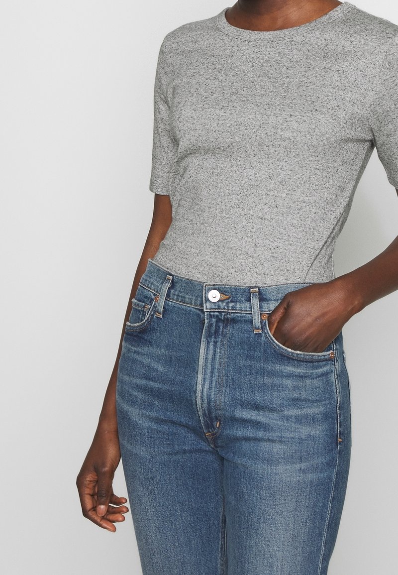 T-shirt gris à manches courtes en tricot texturé, associé à un jean bleu taille haute avec une conception classique à cinq poches et une fermeture à boutons.
