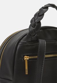 Sort lædertaske med en struktureret overflade, udstyret med et flettet håndtag, guld lynlås og en udvendig lynlåslomme med en pull-tab.