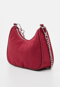 Rød nylon skuldertaske med en buet form, sølv kædestropp og top lynlåslukning. Glat tekstur med minimale syninger.