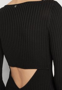 Top nero a costine con scollatura ampia, dettagli con cut-out sulla schiena e un piccolo logo vicino al collo.