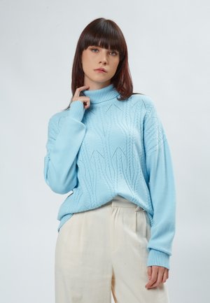 Helles blaues gestricktes Rollkragensweatshirt mit einem strukturierten Muster und gerippten Bündchen, kombiniert mit cremefarbenen, hochtaillierten Hosen.