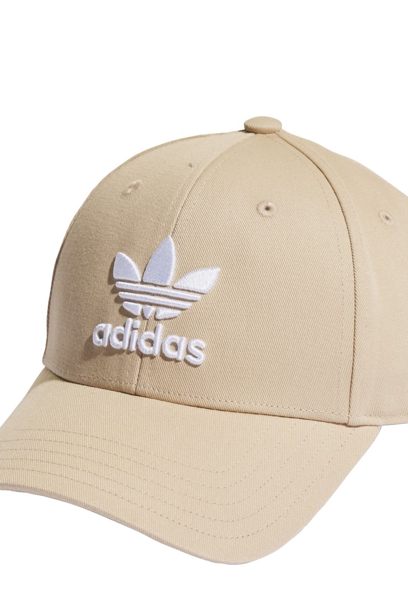 Gorra de béisbol beige hecha de tela texturizada, con un logotipo de Adidas bordado en blanco que presenta tres franjas y una corona redondeada.