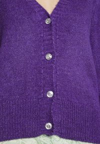 Lila V-ringad kofta i mjukt stickat material, med sex glänsande, klara knappar och ribbade detaljer vid fåll och ärmar.