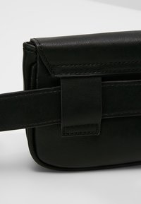 Sac bandoulière en cuir noir avec une texture lisse, une forme rectangulaire, et un rabat avec une attache à sangle.